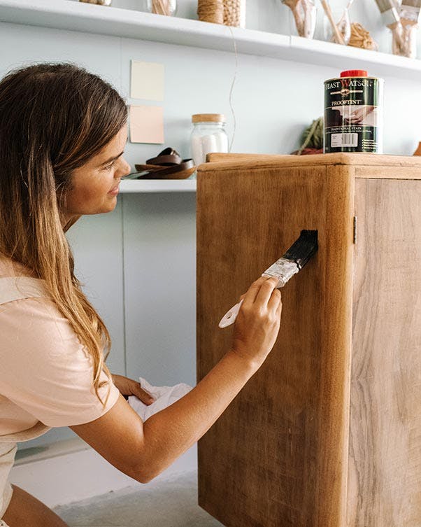 Geneva Vanderzeil applying Prooftint stain to a vintage cabinet